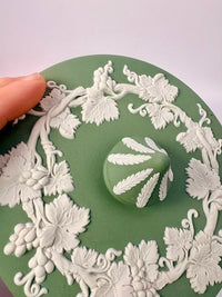 Decorative green plate with white floral patterns and a handprint design, held by a hand.