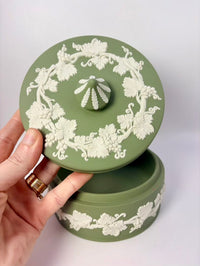 Green ceramic container with white floral patterns held by a hand on a light gray background
