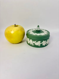 Green decorative box with white floral patterns next to a yellow apple on a white background
