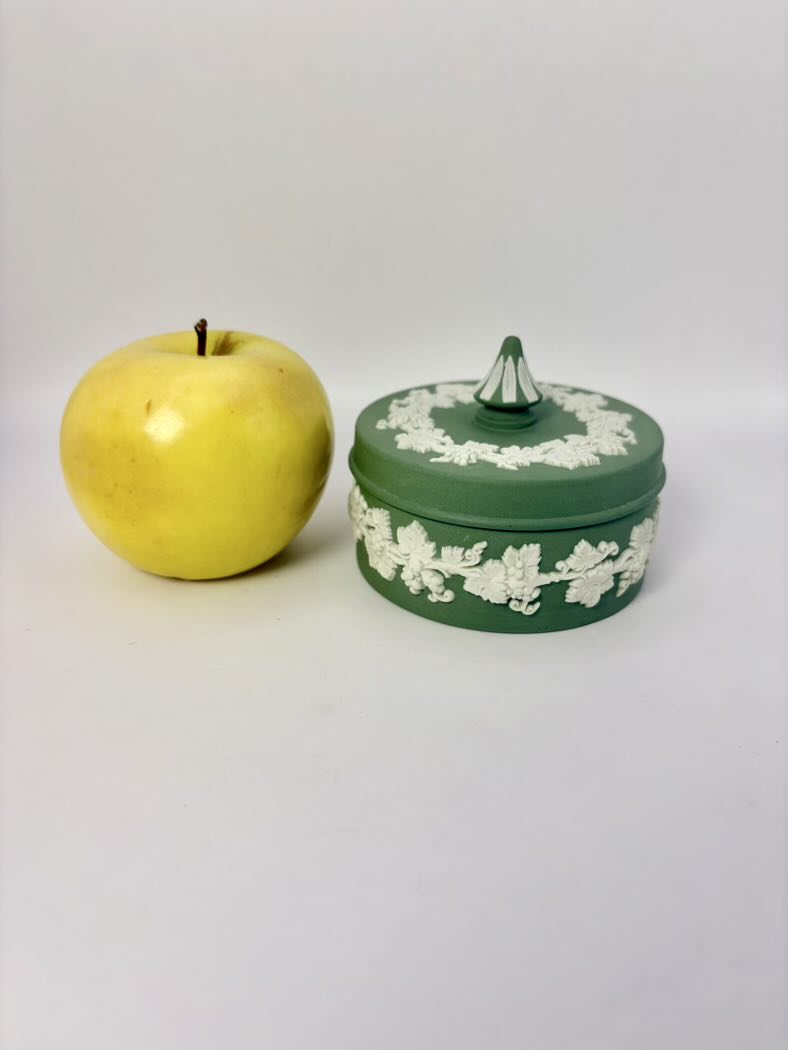 Green decorative box with white floral patterns next to a yellow apple on a white background