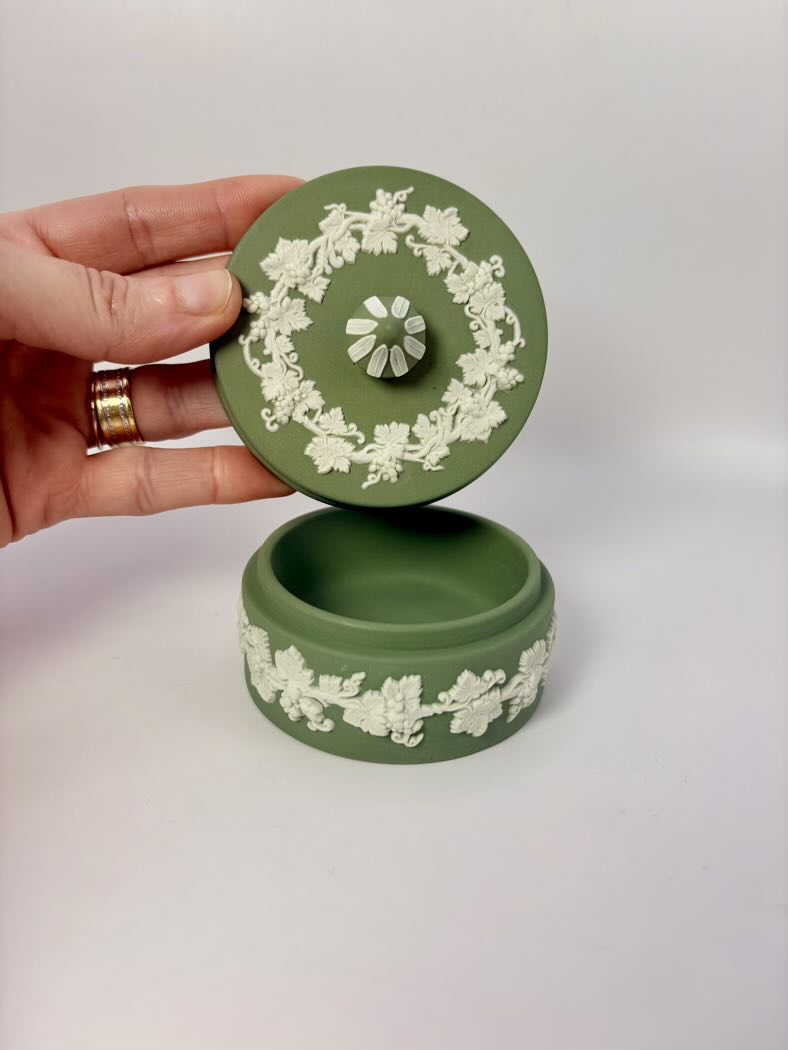Green decorative box with white floral patterns held by a hand on a white background
