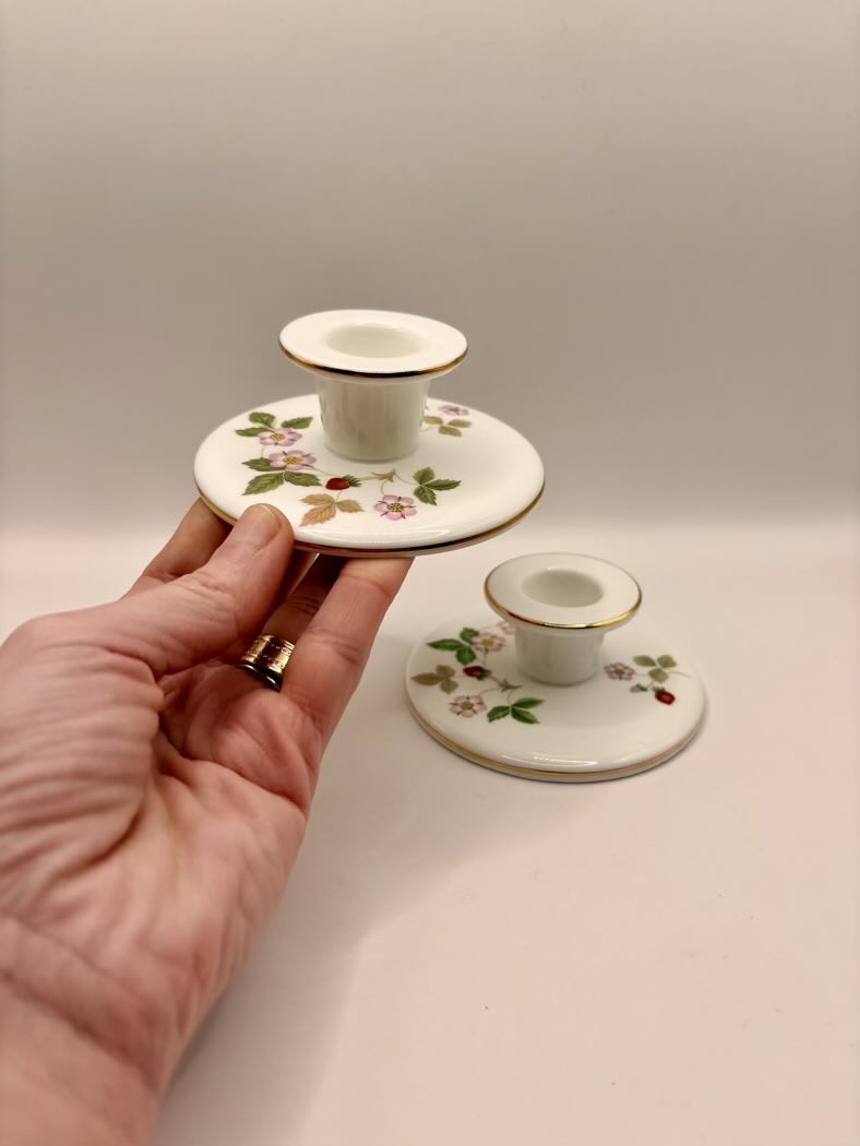 Hand holding a small decorative ceramic candle holder with floral patterns on a plain background
