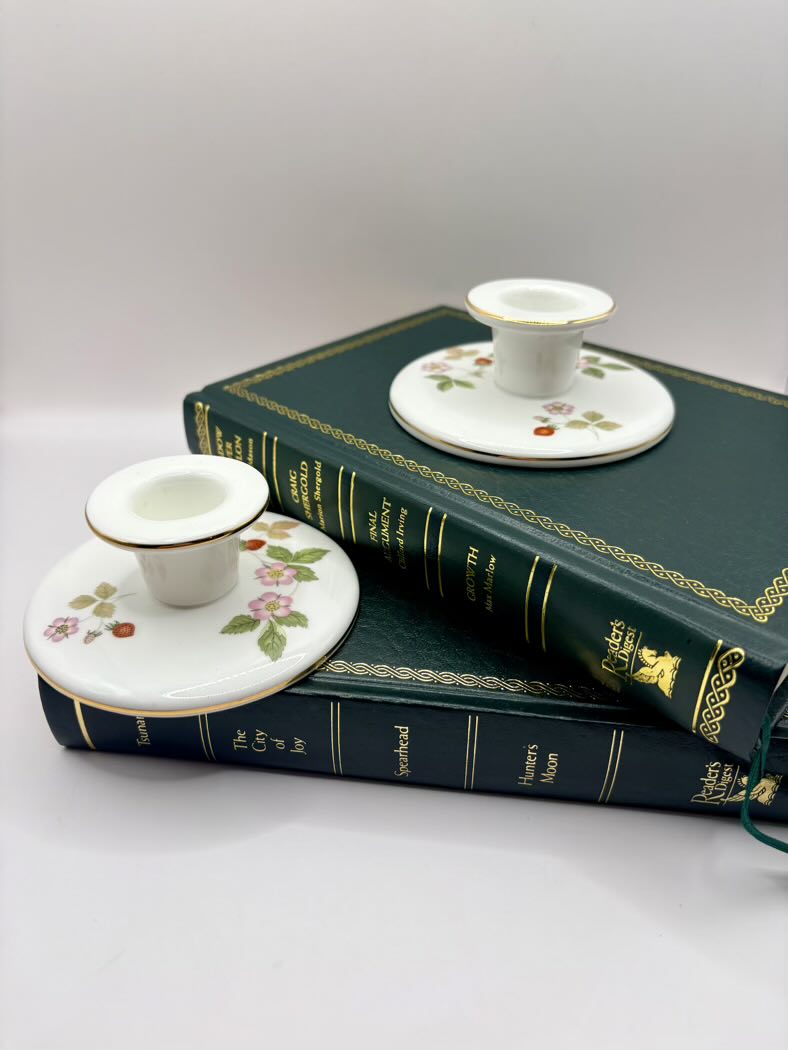 Two small white ceramic candle holders with floral designs on top of a green book.
