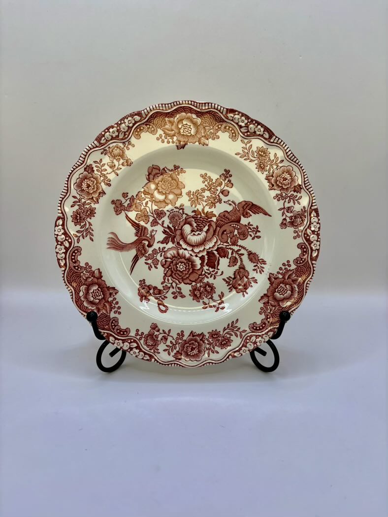 Decorative plate with red floral and bird pattern on a stand against a white background