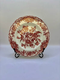 Decorative plate with red floral and bird pattern on a stand against a white background