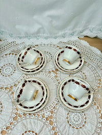 Set of four white teacups with gold accents on a lace tablecloth.