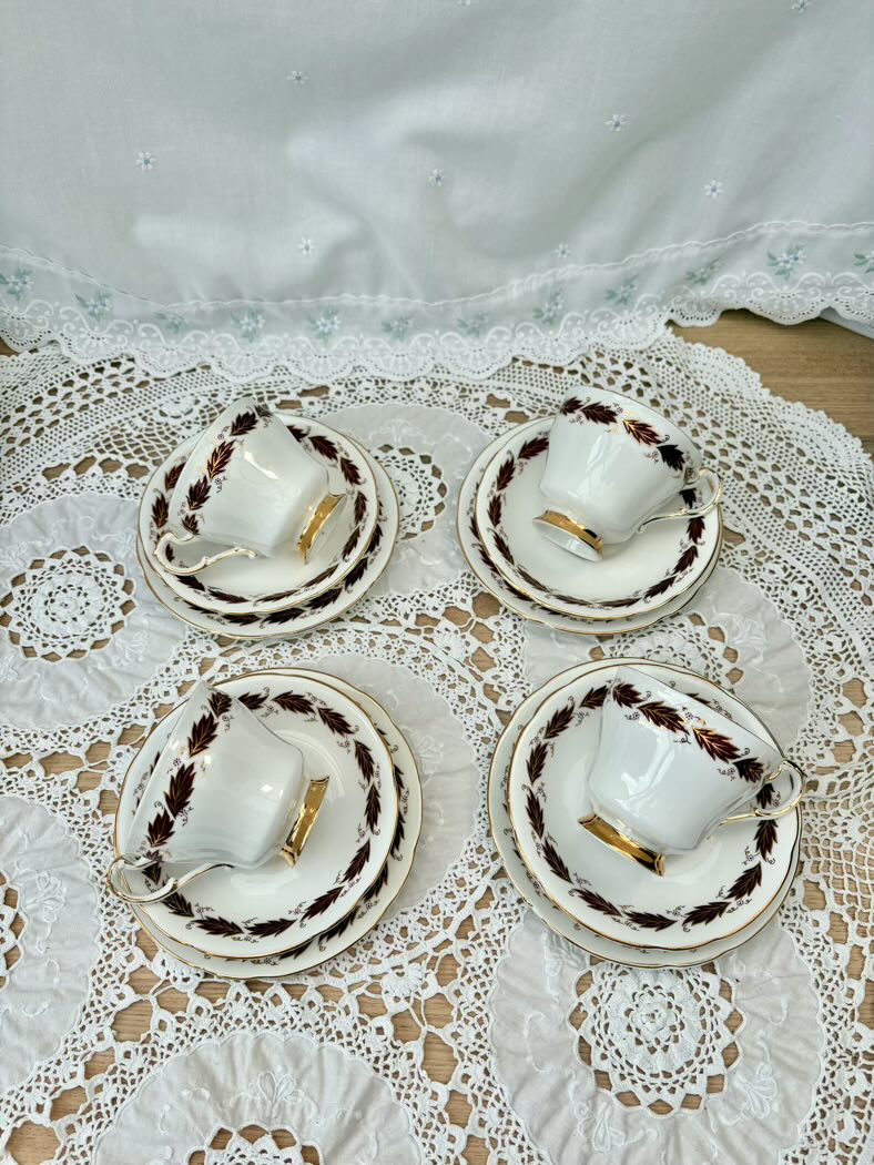 Set of four white teacups with gold accents on a lace tablecloth.