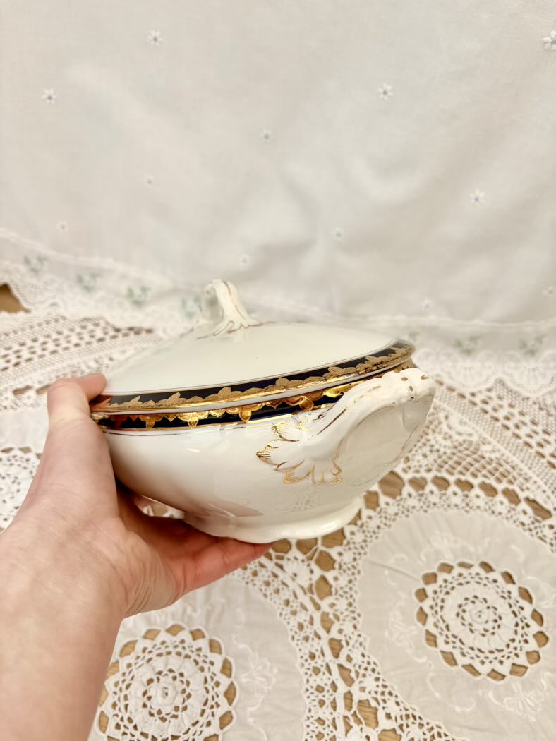 Hand holding a decorative white bowl with gold trim on a lace tablecloth.