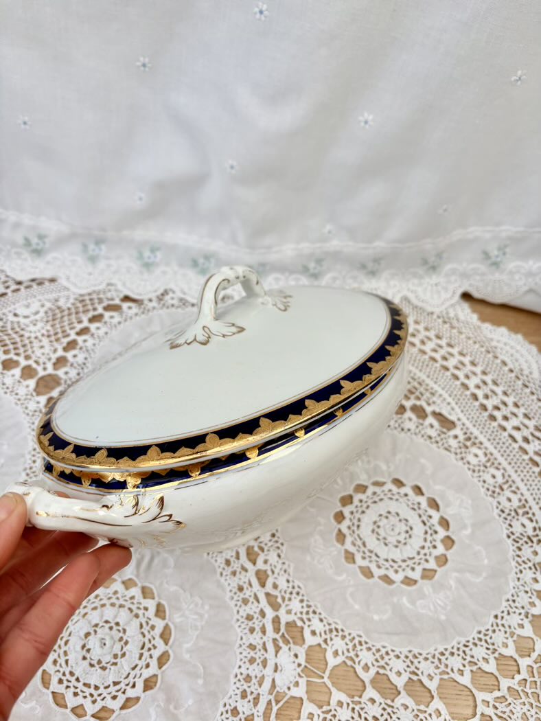 Decorative white dish with gold trim held over a lace tablecloth