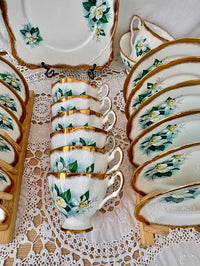 Set of ceramic teacups and plates with floral design on a lace tablecloth.
