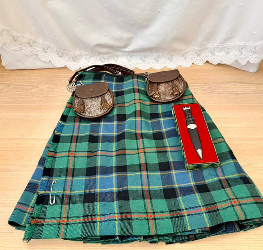 Green plaid kilt with accessories on a wooden surface and white curtain background