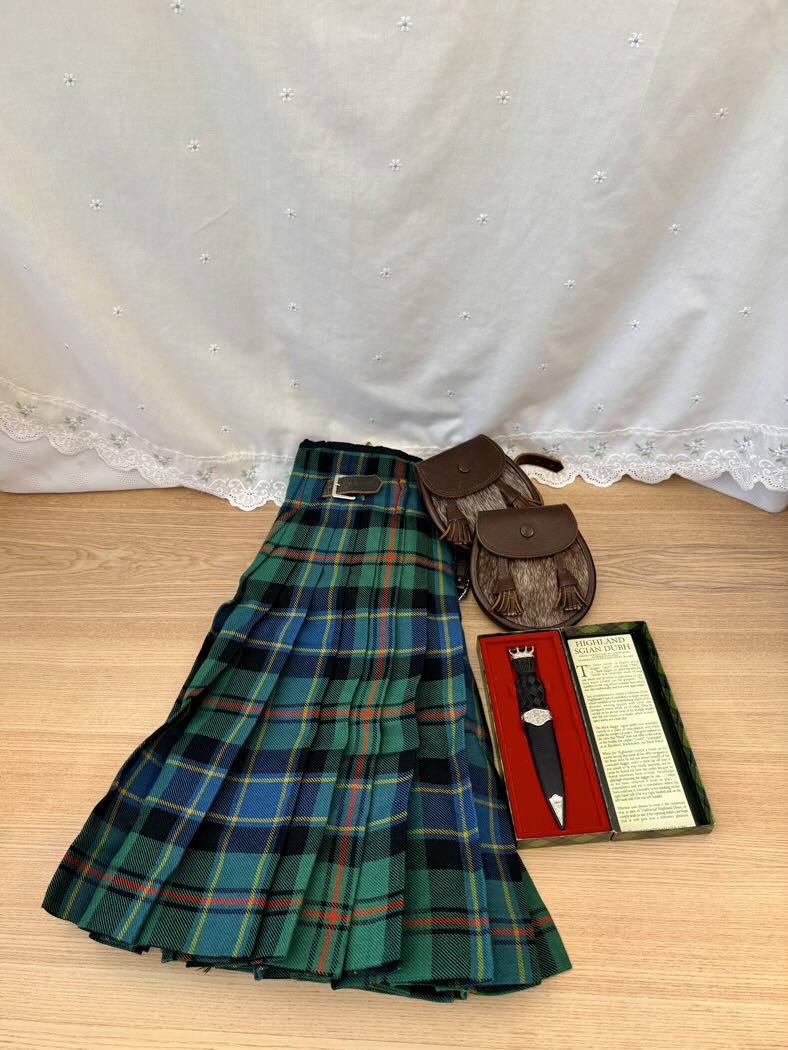 Green plaid kilt with accessories on a wooden surface and white lace curtain background