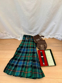 Green plaid kilt with accessories on a wooden surface and white lace curtain background