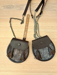 Two brown leather crossbody bags with fringe on a wooden surface, accompanied by a ruler for size reference.