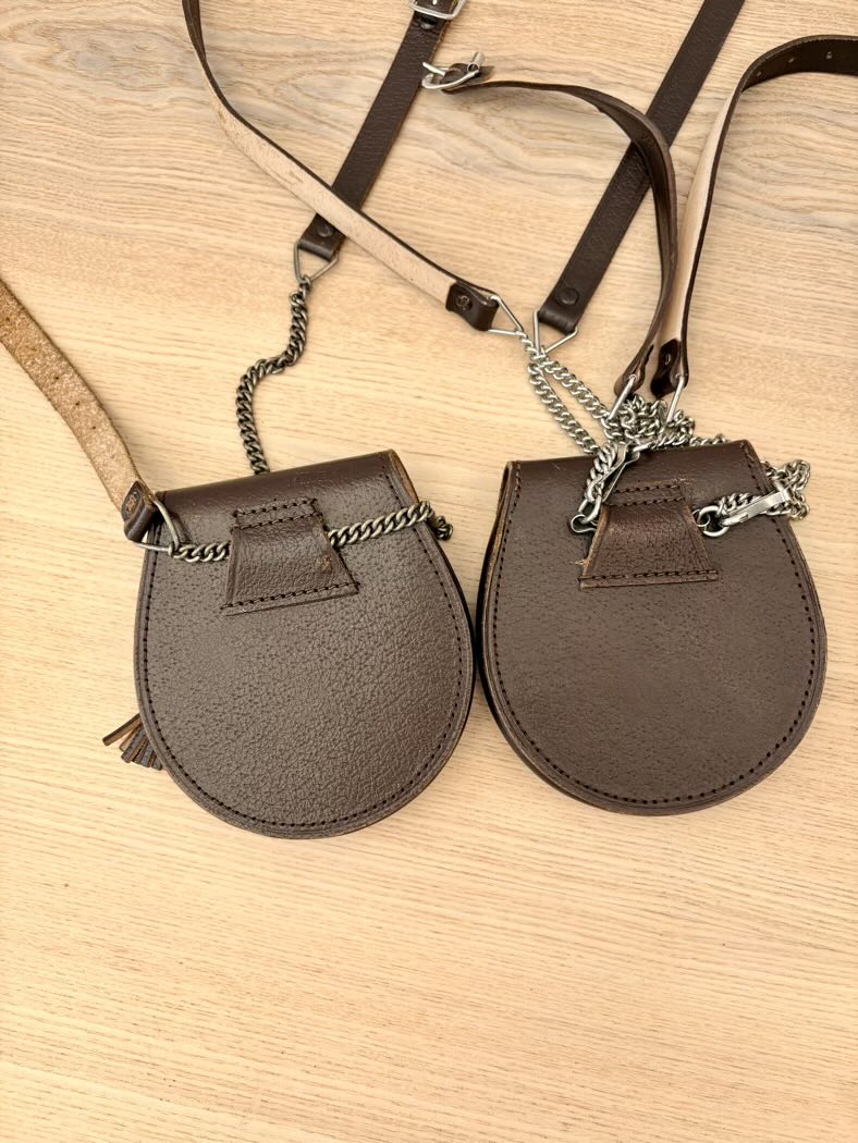 Two brown leather crossbody bags with chains on a wooden surface