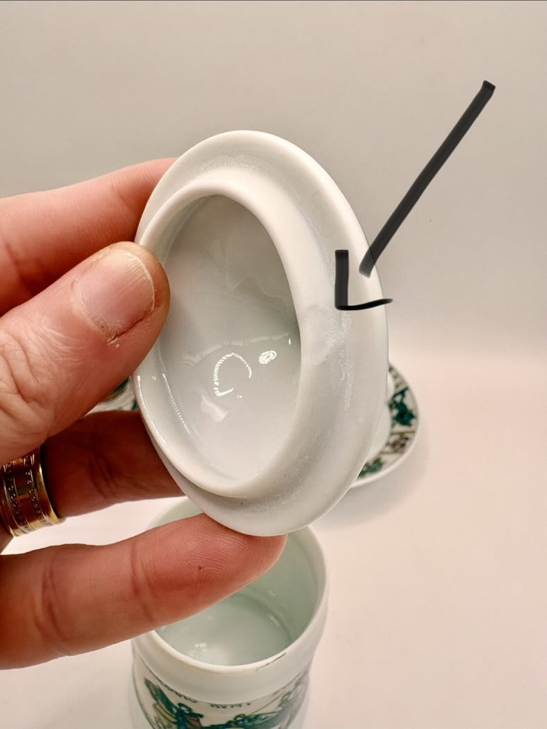 Hand holding a white ceramic container with a lid, showing a small amount of liquid inside.