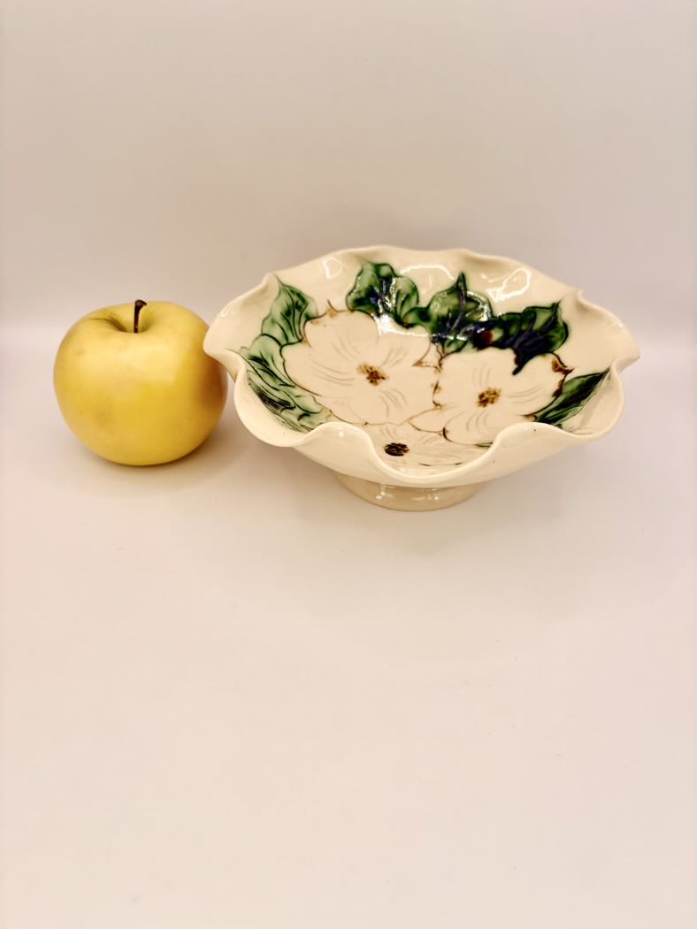 Decorative ceramic bowl with floral design next to a yellow apple on a white background
