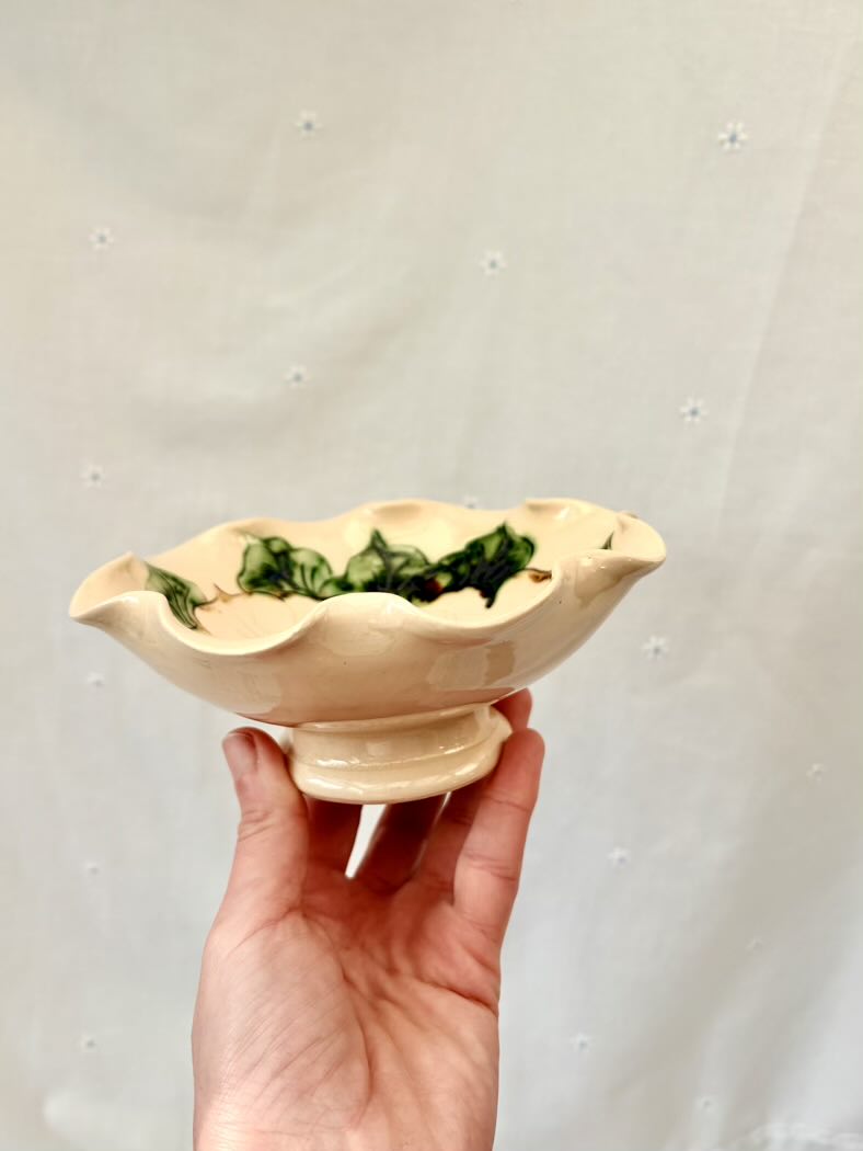Hand holding a small ceramic bowl with green leaves against a light gray background