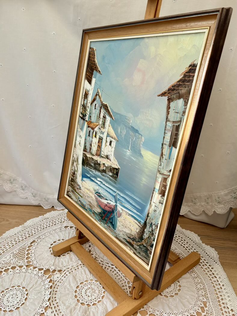 Framed painting of a coastal scene on a lace-covered surface