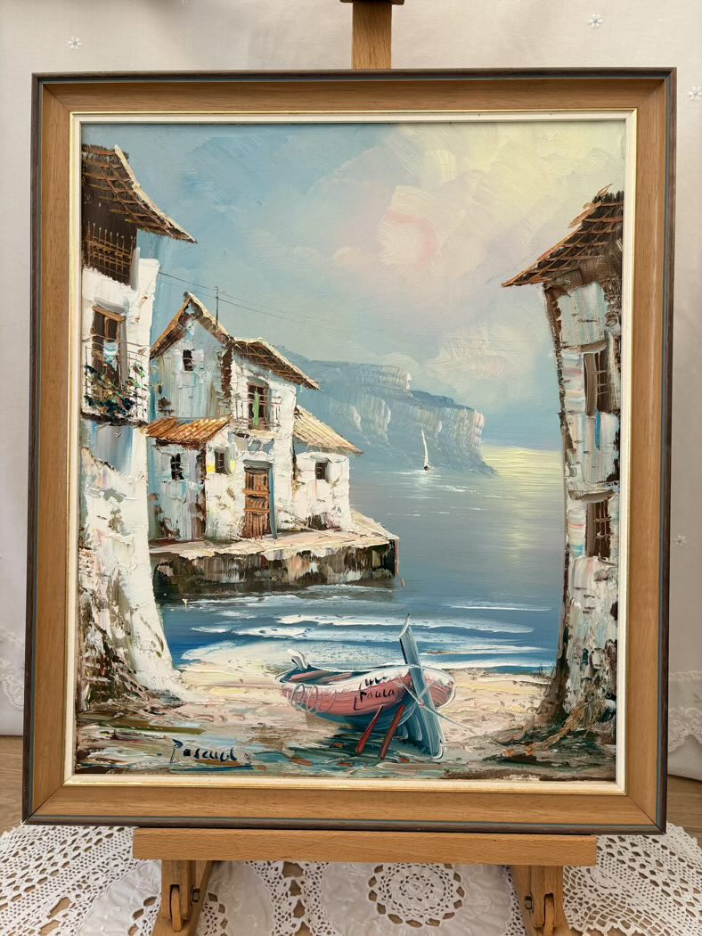 Framed painting of a coastal scene with houses and a boat.