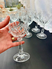 Hand holding a crystal wine glass with more glasses in the background on a reflective surface