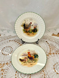 Two ceramic plates with rooster designs on a lace tablecloth.