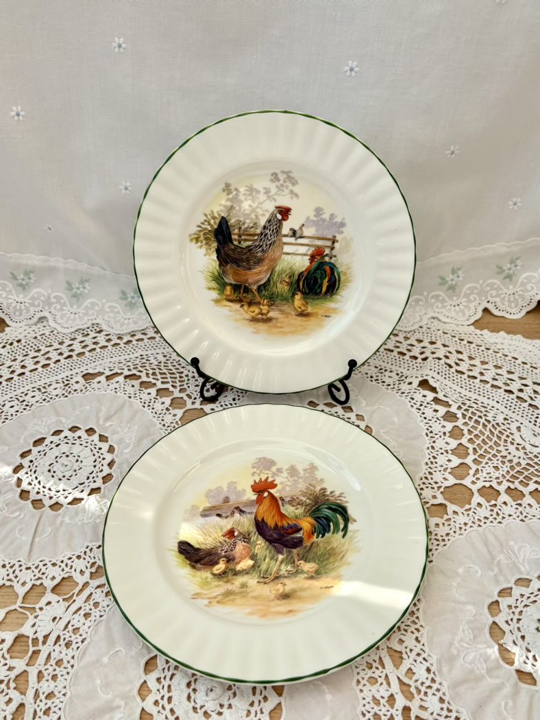 Two ceramic plates with rooster designs on a lace tablecloth.