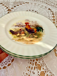 Decorative plate with a rooster design held over a lace tablecloth