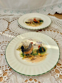 Two decorative plates with rooster designs on a lace tablecloth.