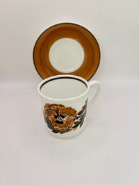 Ceramic mug with floral design and matching saucer on a light gray background
