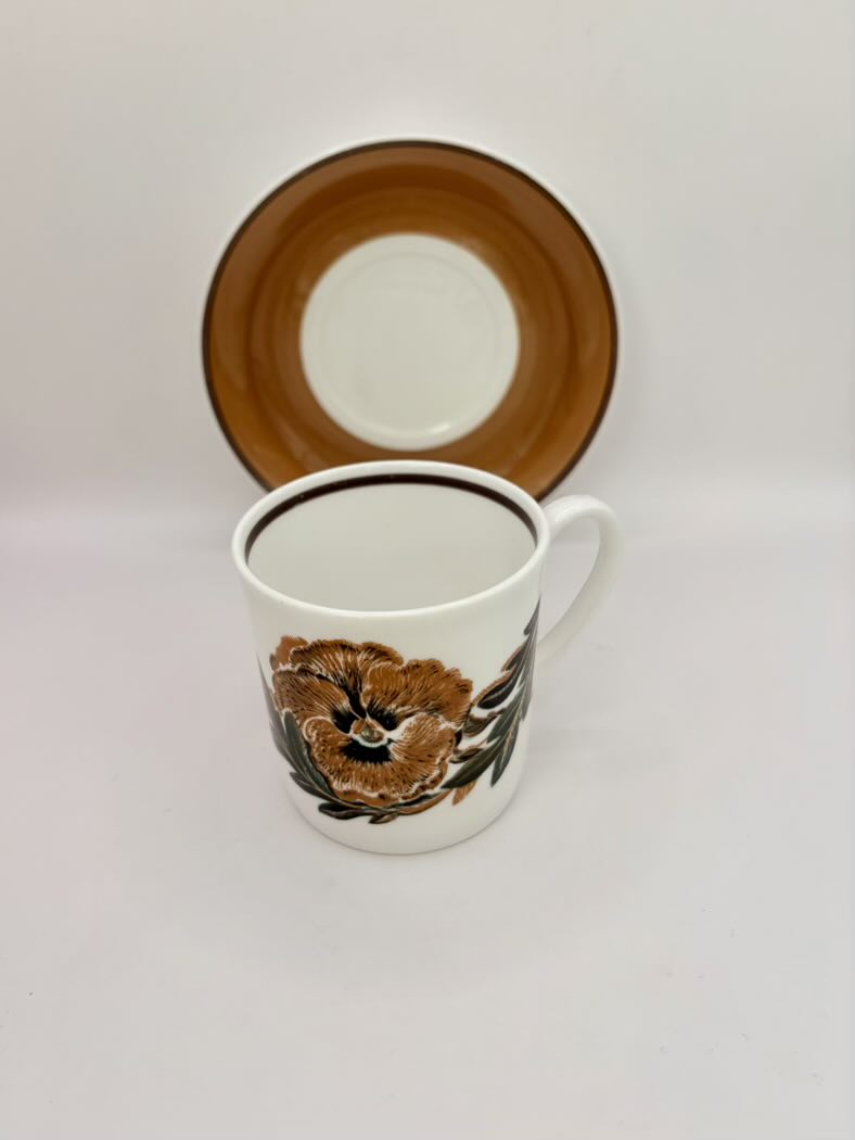 Ceramic mug with floral design and matching saucer on a light gray background