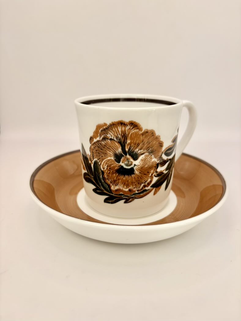 Ceramic mug with floral design on a matching saucer against a plain background