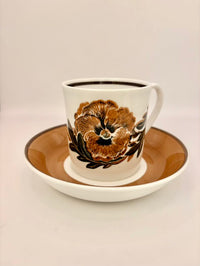 Ceramic mug with floral design on a matching saucer against a plain background