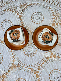 Two ceramic plates with floral designs on a lace tablecloth