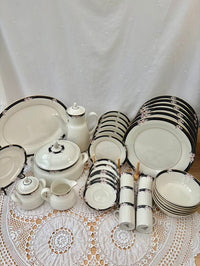 Set of white ceramic dinnerware with black trim on a lace tablecloth.