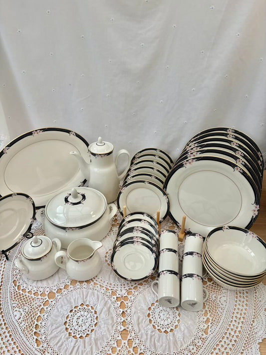 Set of white ceramic dinnerware with black trim on a lace tablecloth.