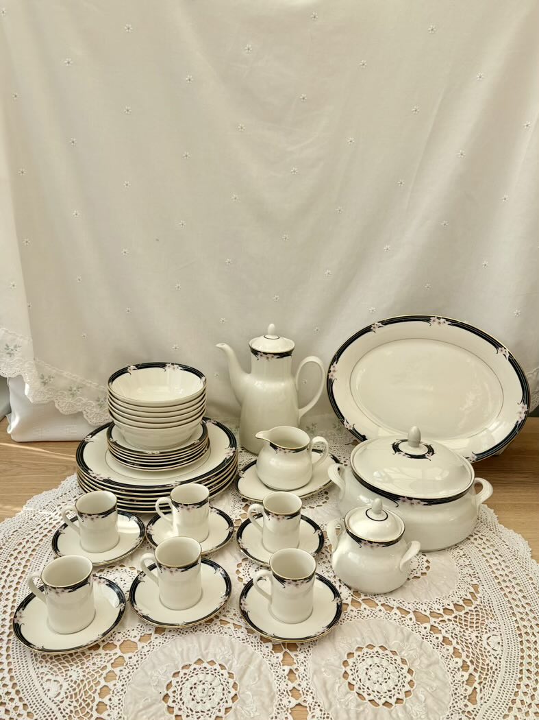 Set of white ceramic tableware with black trim on a lace tablecloth.