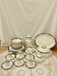 Set of white ceramic tableware with black trim on a lace tablecloth.