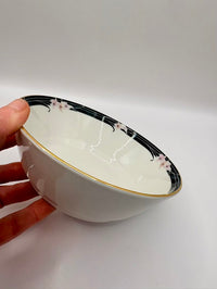 White ceramic bowl with black floral design held by a hand on a white background