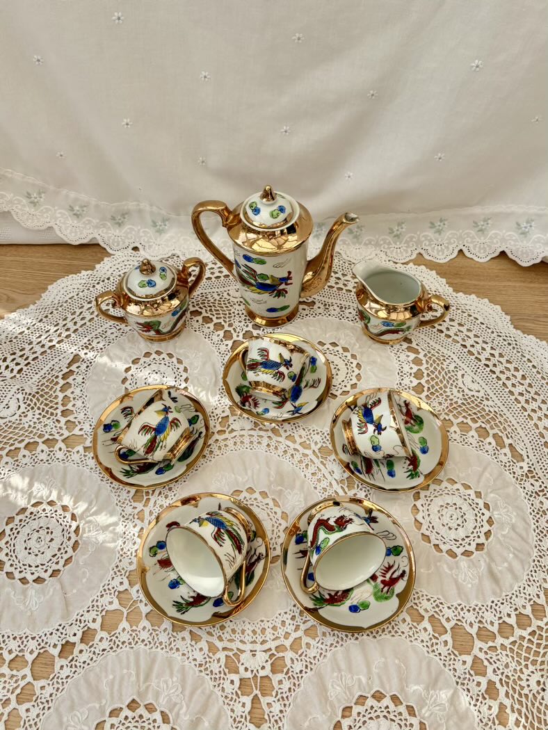 Tea set with decorative teapot, cups, and saucers on a lace tablecloth.