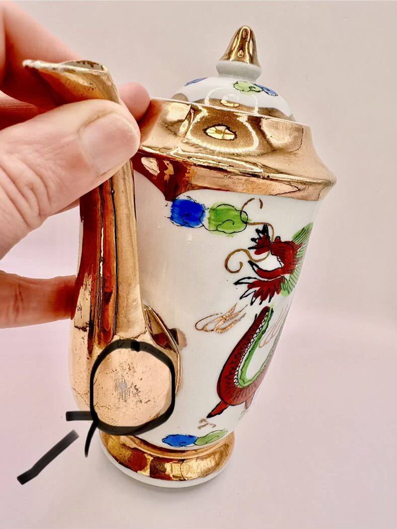 Decorative ceramic container with gold accents and colorful designs held by a hand against a light background