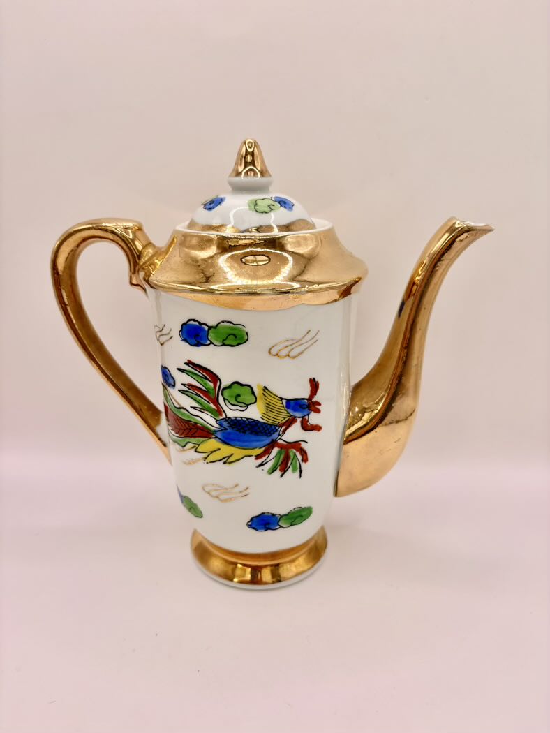 Decorative teapot with gold accents and colorful designs on a light pink background