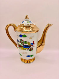 Decorative teapot with gold accents and colorful designs on a light pink background