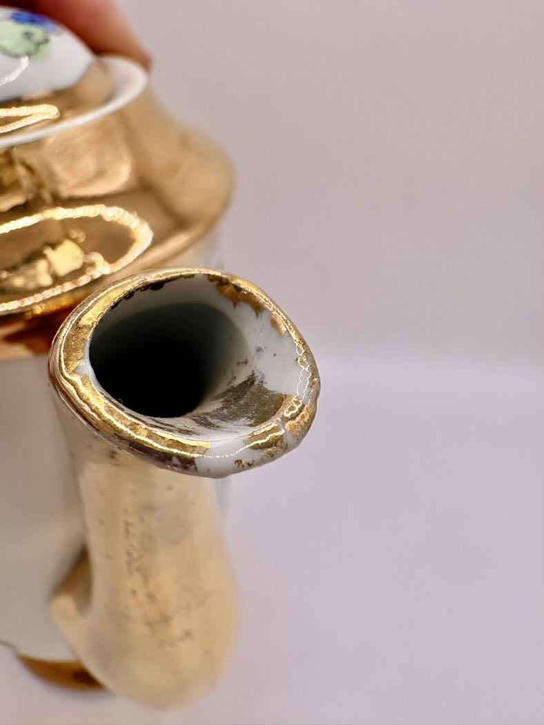 Close-up of a ceramic teapot with gold trim on a plain background