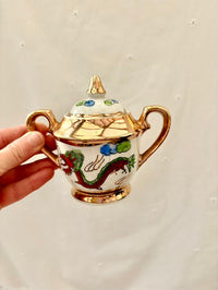 Small decorative teapot with dragon design held by a hand against a plain background