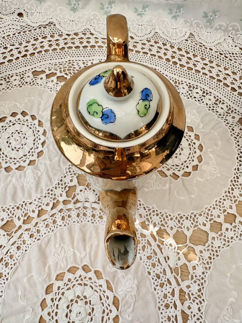 Decorative teapot with a white shade featuring colorful floral patterns on a lace tablecloth.