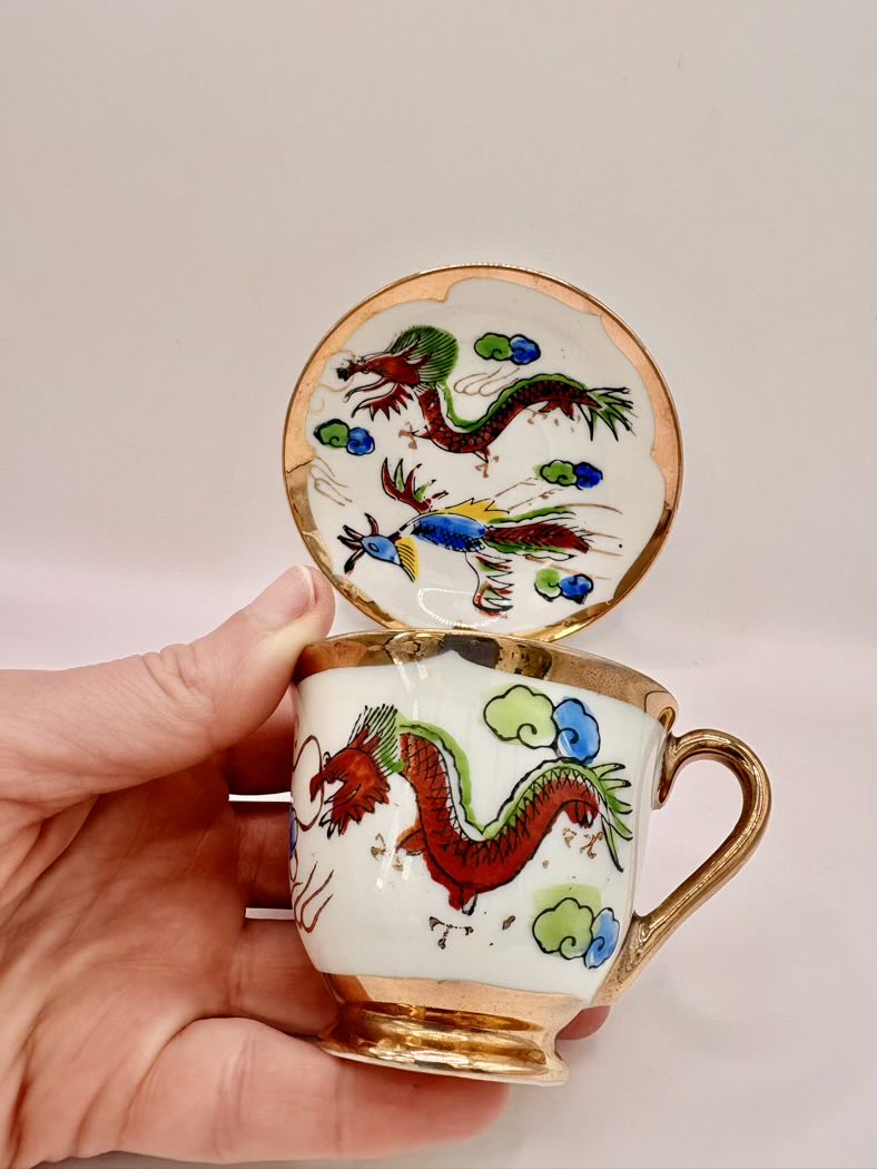 Decorative teacup with dragon design held by a hand against a plain background