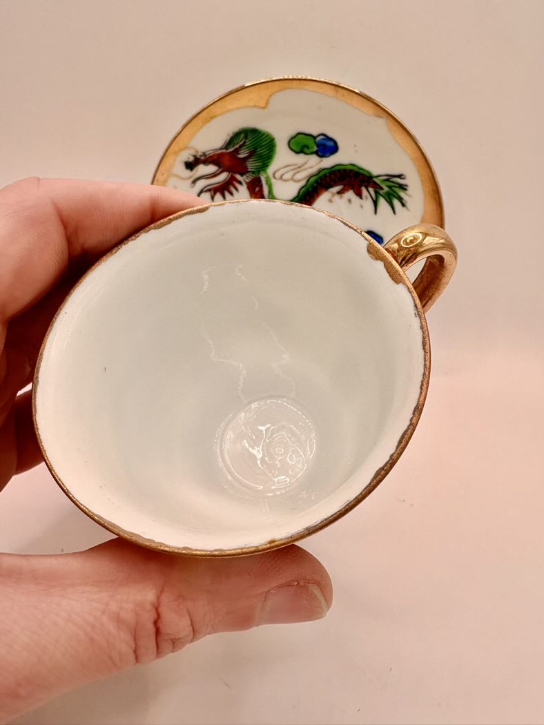 Small decorative cup with gold rim and colorful design held by a hand against a plain background