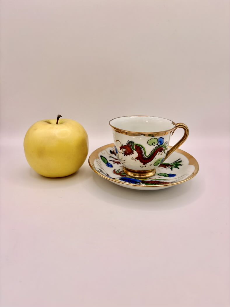 Teacup with decorative handle and saucer next to a yellow apple on a plain background