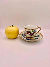 Teacup with decorative handle and saucer next to a yellow apple on a plain background